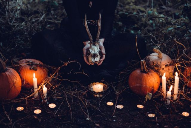 hands holding a skull with candles and pumpkin