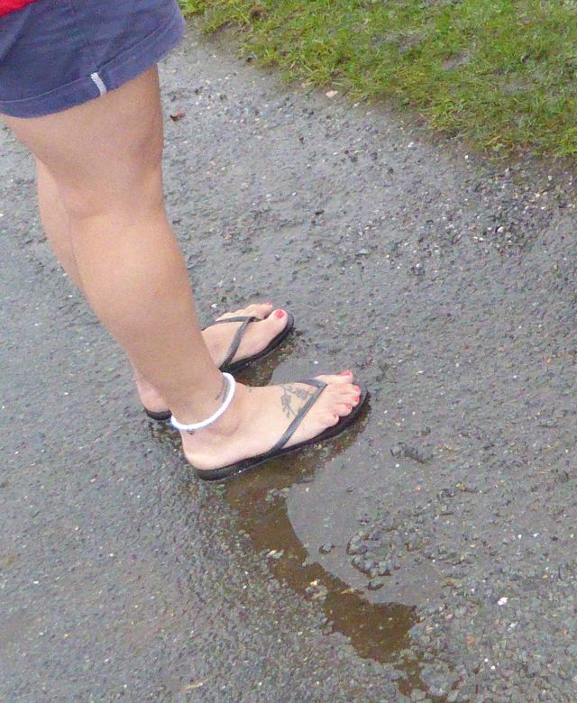 Wetterunempfindlich nackte Frauenbeine und Füße in Flipflops im Regen. Warum frieren Britinnen nicht?
