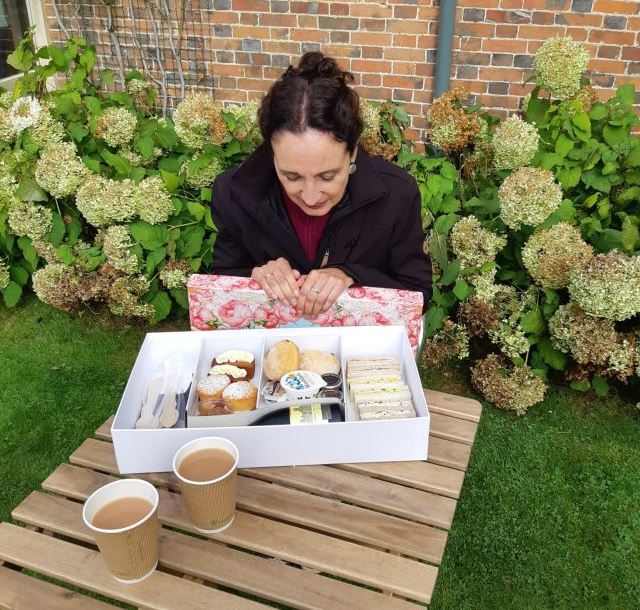 Box mit Afternoon Tea und 2 Tassen Frau vor Blumen