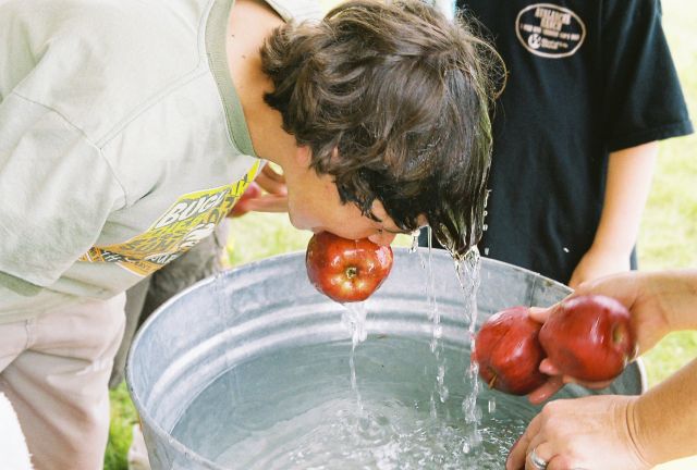 Junge mit nassem Haar beim Apple Bobbin' Partyspiel an Halloween Äpfel und Wasserzuber